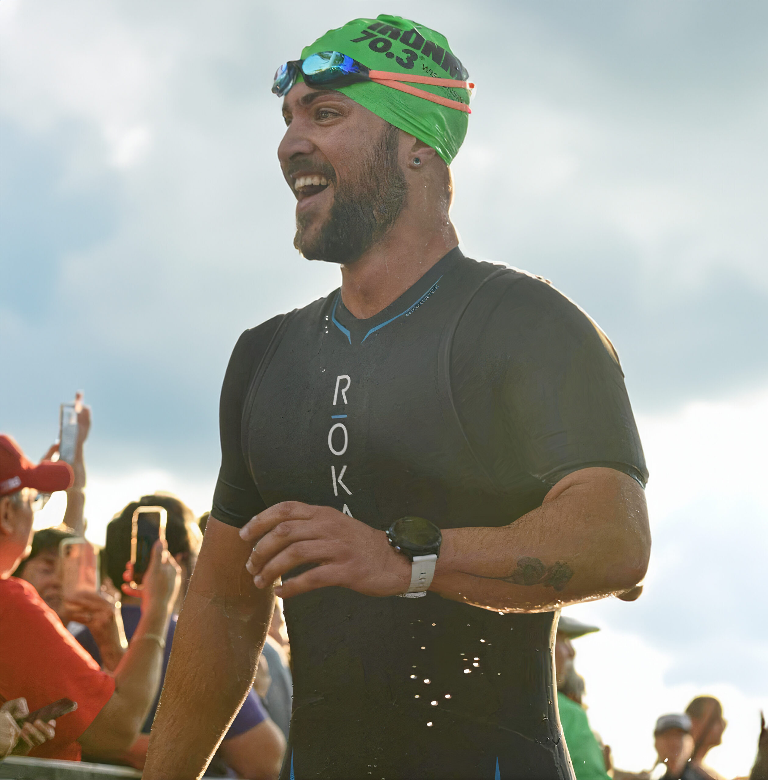 Triathlon coach Nick Savin, exuberant with accomplishment, emerges from the water in a wetsuit and swim cap, reflecting the active, hands-on coaching style at Run Strength Academy.